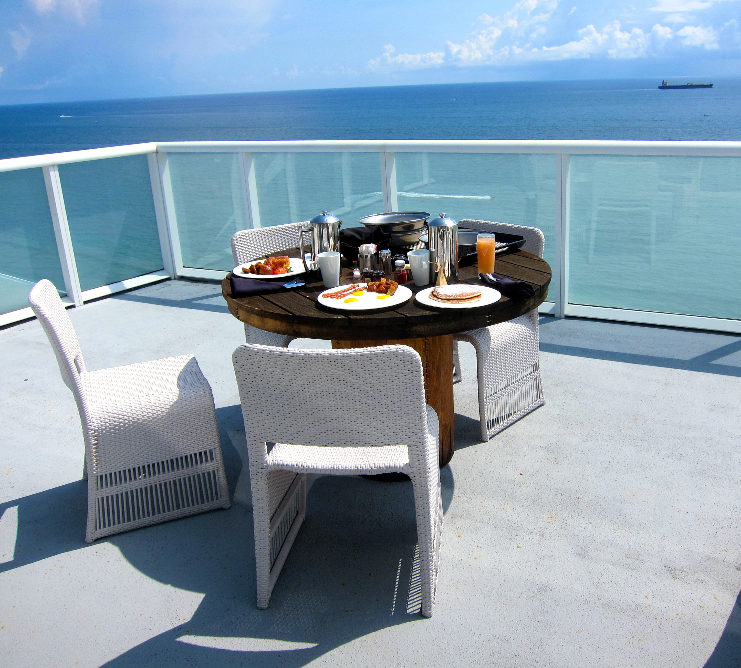 a table with food on it and chairs on a deck overlooking the ocean