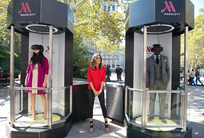 a woman standing in a booth with a man and a woman wearing virtual reality headsets