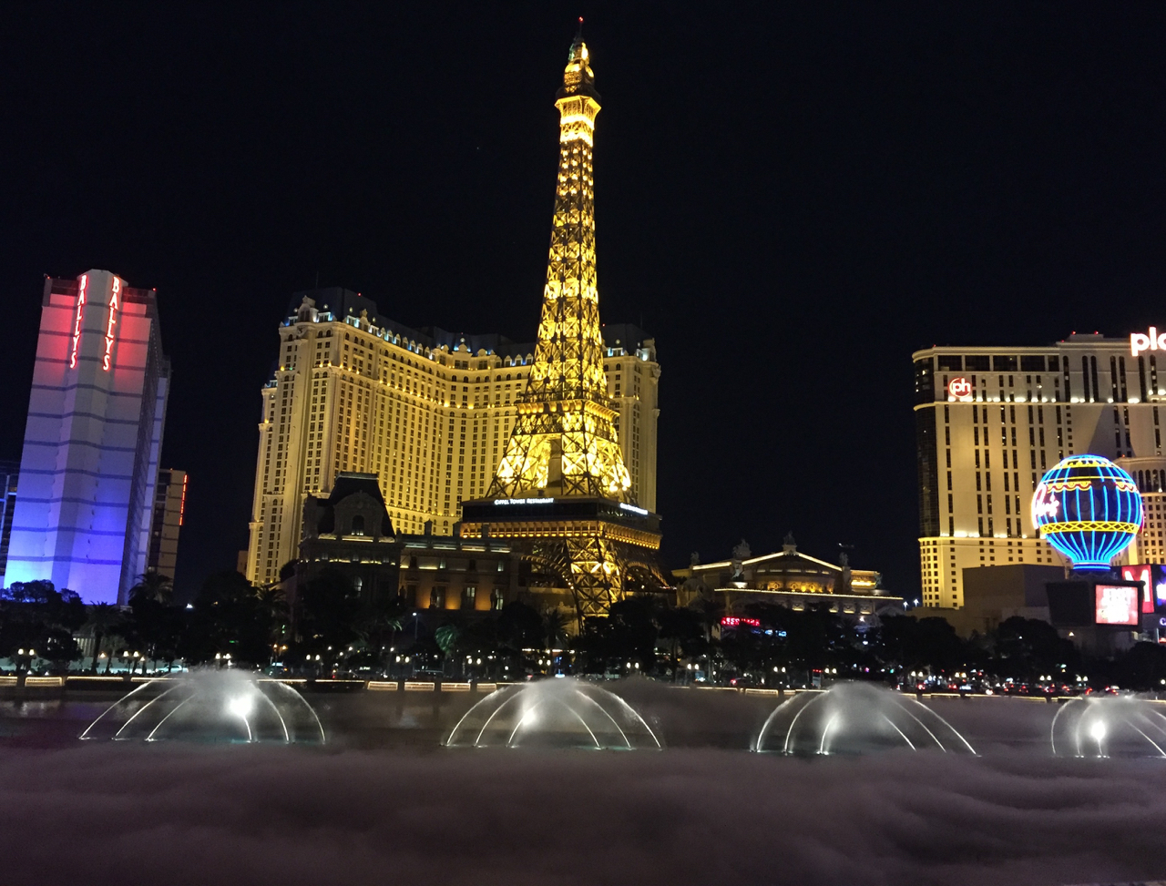 a large tower lit up at night with Paris Las Vegas in the background