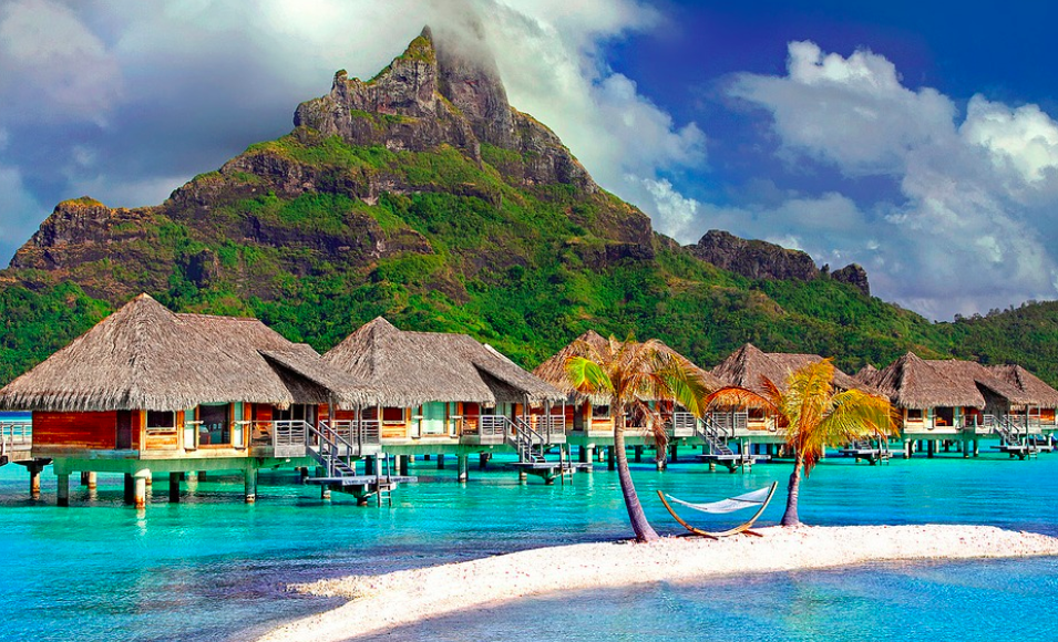 a group of houses on a beach with palm trees and Bora Bora in the background